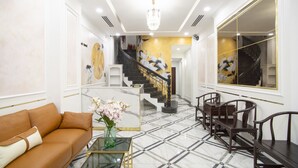 Een moderne lobby met een marmeren vloer, een bank, een glazen bijzettafeltje en een trap met een muurschildering.