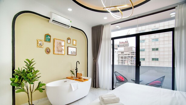 Een moderne hotelkamer met een groot bed, een vrijstaand bad, een potplant en uitzicht op de stad door grote ramen.