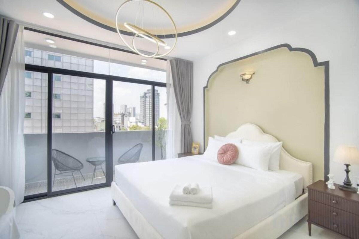 Une chambre d’hôtel avec un grand lit, un balcon avec des chaises et une vue sur la ville.