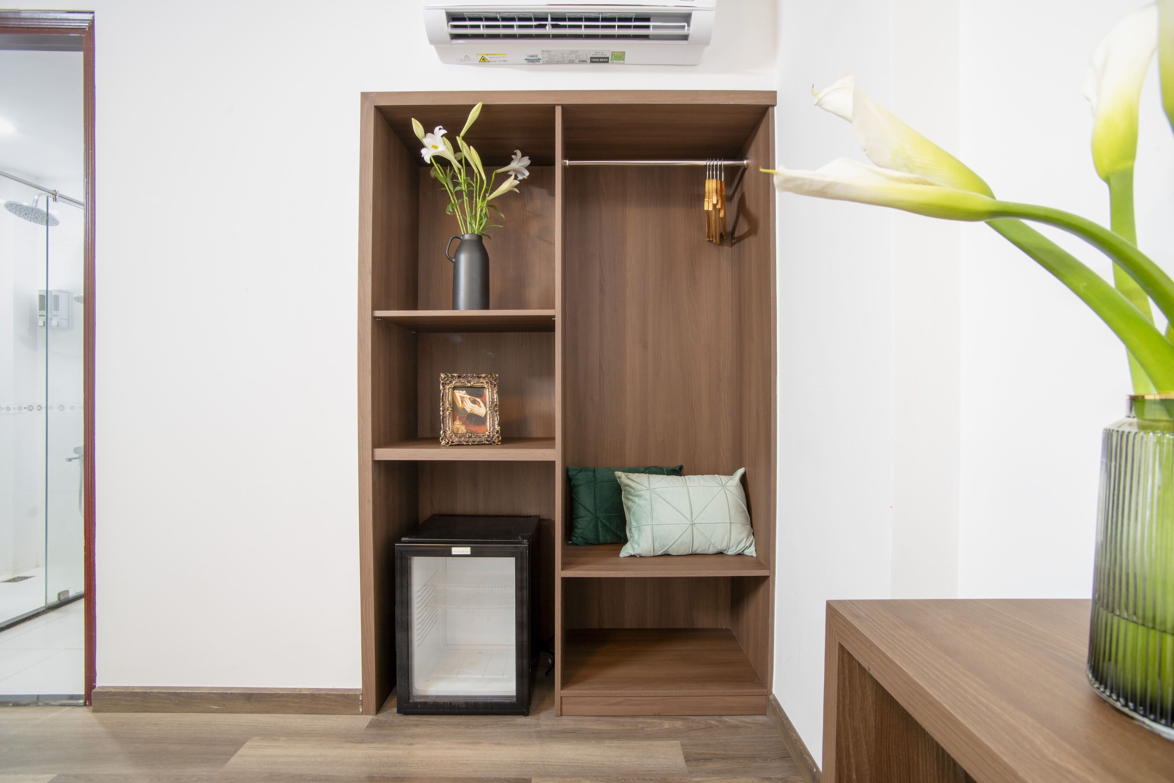 Un baño moderno con cabina de ducha de vidrio, tocador de madera y unidad de almacenamiento empotrada con estantes y un refrigerador pequeño.