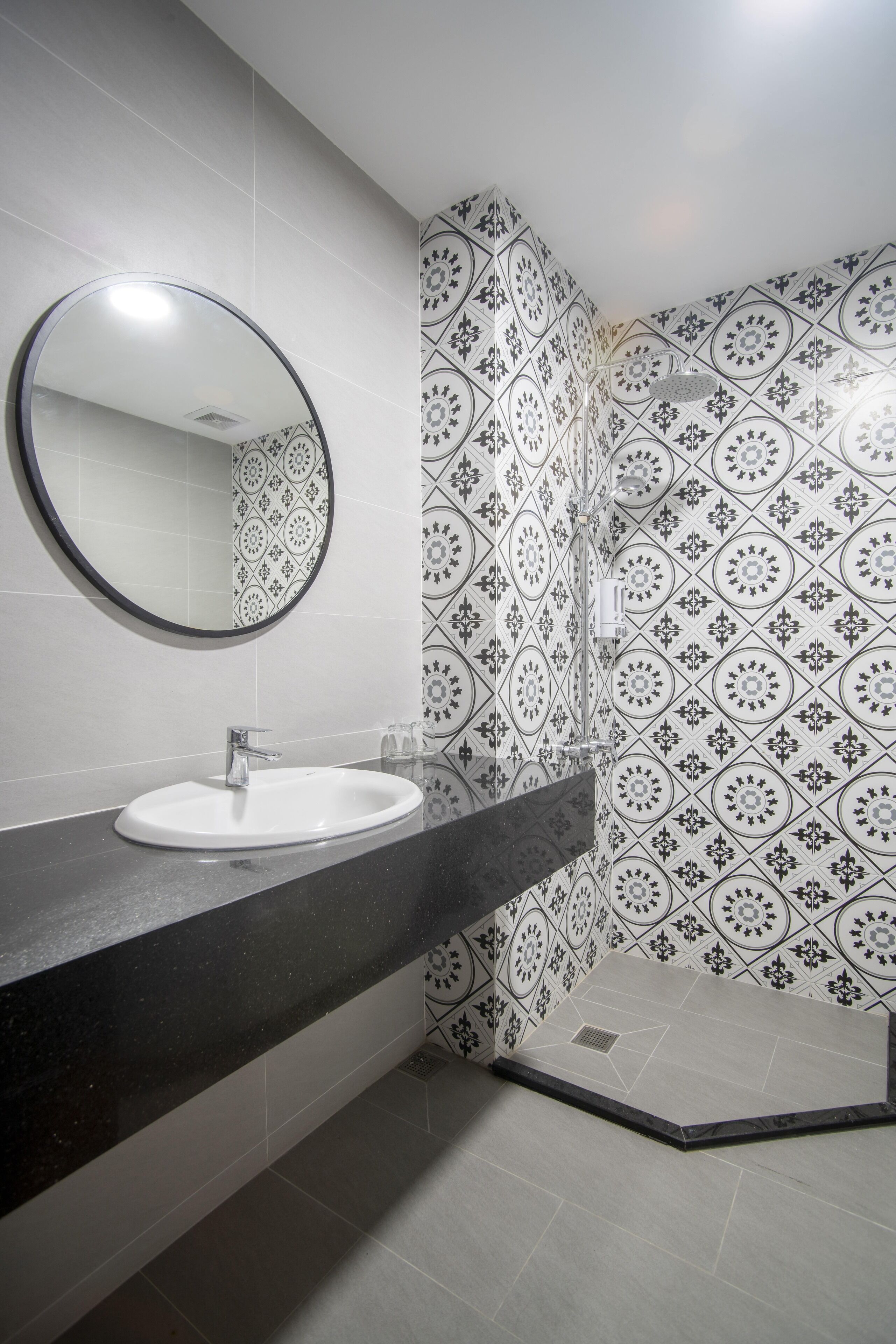 A bathroom with a white sink, a round mirror, and patterned tiles on the walls and floor.