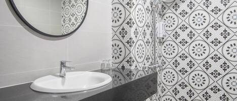 A bathroom with a white sink, a round mirror, and patterned tiles on the walls and floor.