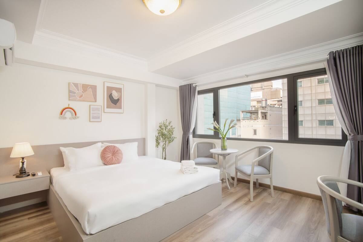 Ein Hotelzimmer mit einem großen Bett, einem kleinen Tisch mit Stühlen, einem Fenster mit Vorhängen und einem Bild an der Wand.