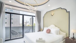 Hotelkamer met een groot bed, een nachtkastje, een lamp, een stoel en uitzicht op de stad door een schuifdeur.
