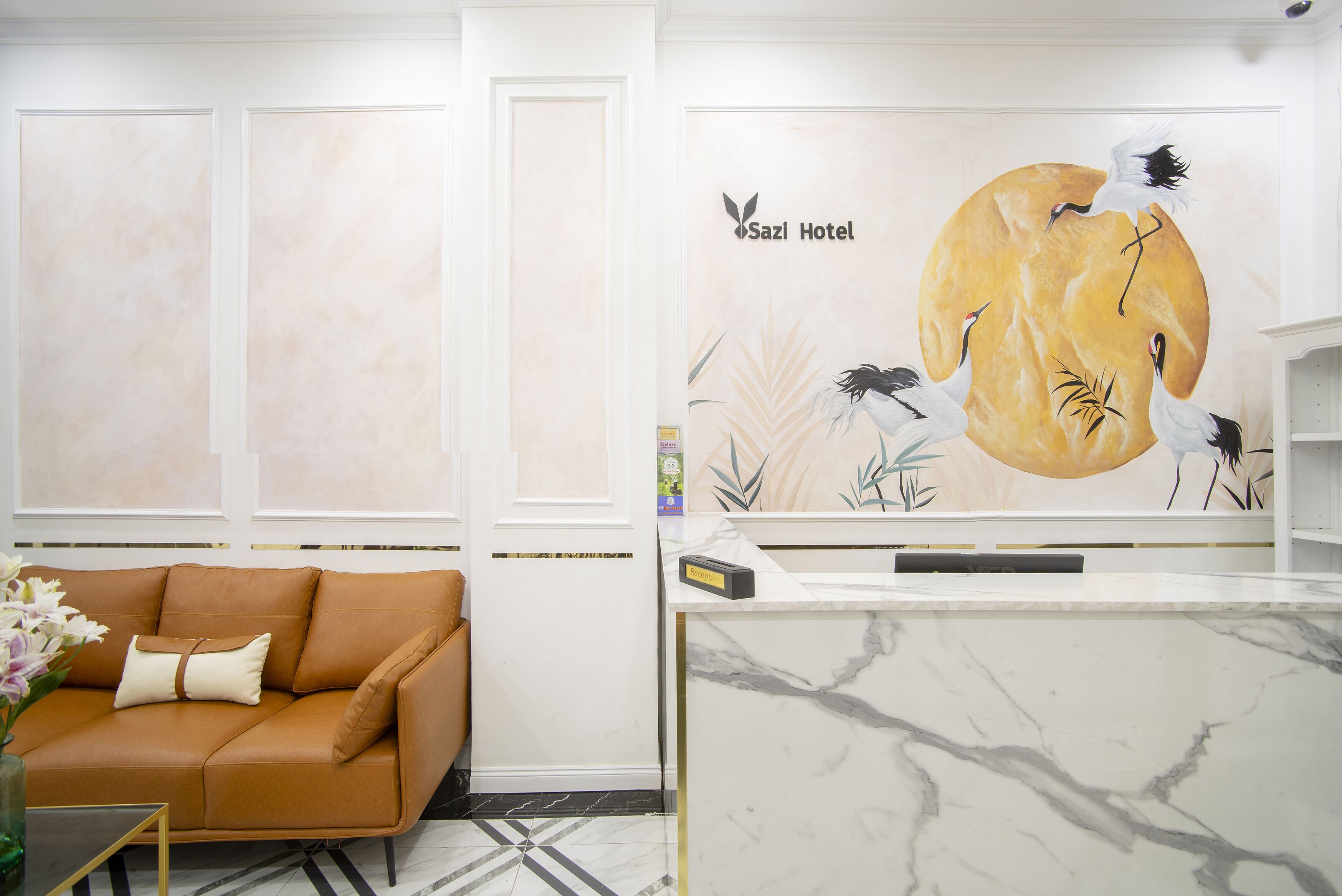 A reception area with a marble counter, a brown sofa with cushions, and a wall mural depicting cranes and foliage.