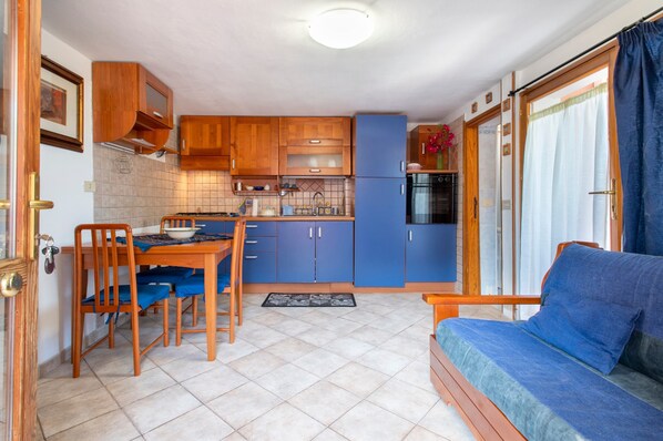 A compact kitchen with blue cabinets, a dining table with chairs, and a sofa.