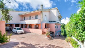 A two-story building with a paved driveway, a parked car, and a potted plant. - Holiday Home 'Casetta Brandinu' with Mountain View, Balcony & Wi-Fi (Sassari)