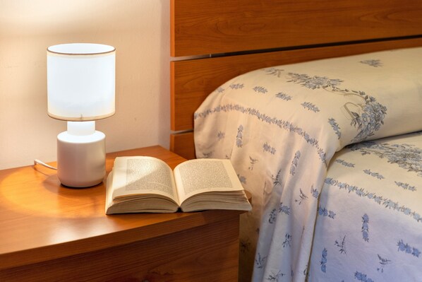 A wooden bedside table with a white lamp and an open book.