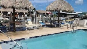 Piscina com espreguiçadeiras e guarda-sóis de palha, cercada por uma grade.