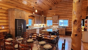 Un acogedor interior de cabaña de madera con una mesa de comedor central tipo isla, armarios de madera, un refrigerador y un letrero de cafetería.
