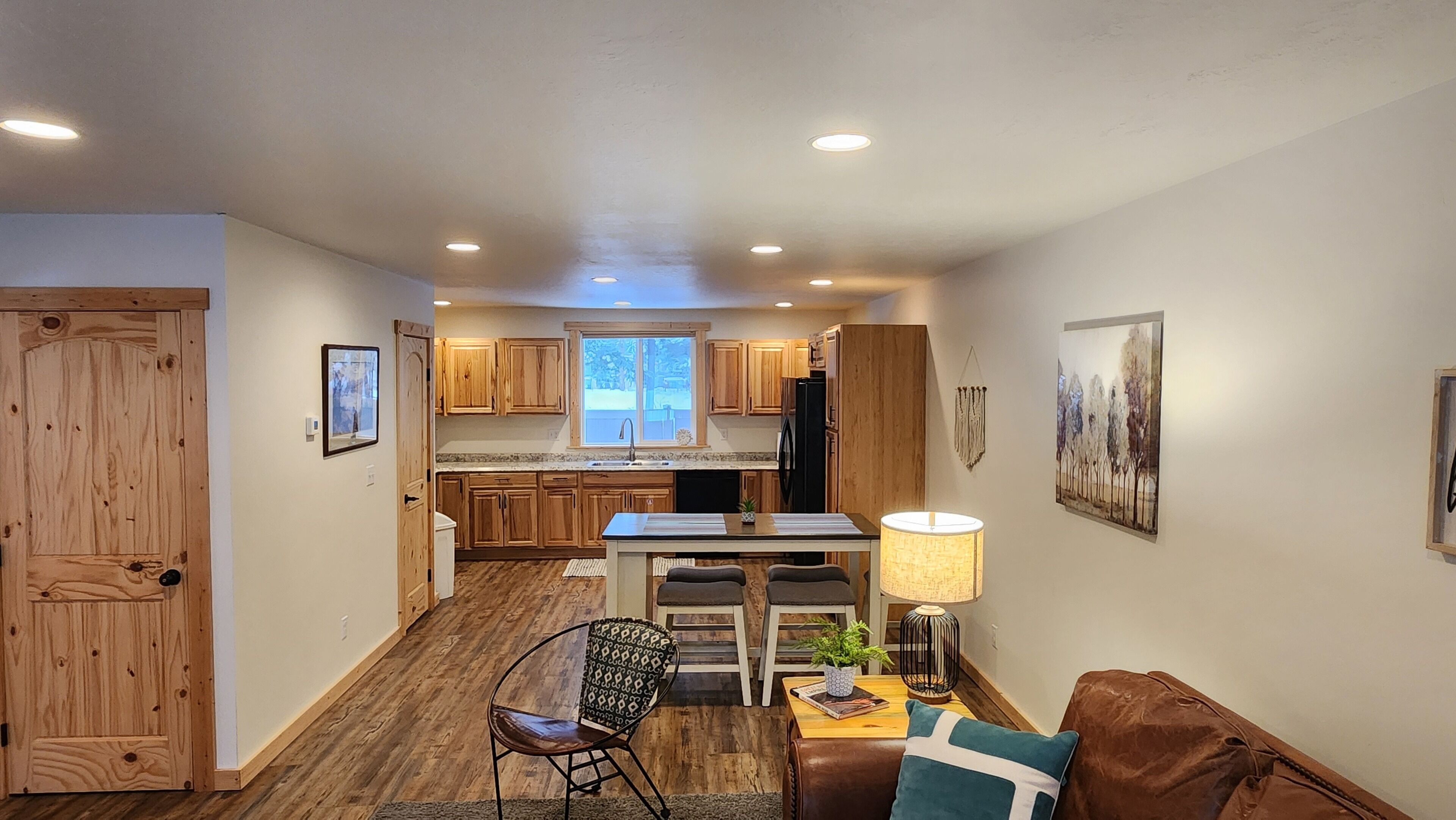 A compact kitchen with wooden cabinets, a dining area with a table and chairs, a sofa, and a lamp.