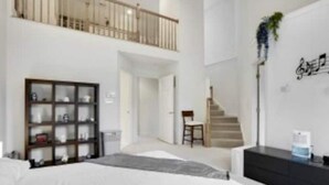Una habitación de hotel moderna con una cama grande, un armario empotrado, una zona de estar y una escalera que conduce a un nivel superior.