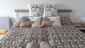 A neatly made bed with a patterned bedspread and two pillows with cartoon faces. - Apartment with panoramic lake view, sauna, close to hiking trails. (Orfu)