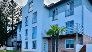 A modern multi-story building with a flat roof, large windows, and a balcony. - Apartment with panoramic lake view, sauna, close to hiking trails. (Orfu)