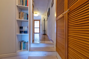 A hallway with a bookshelf, a coat rack, and a door with a wooden shutter.
