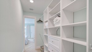 A walk-in closet with white shelving and drawers, a hanging rack, and a visible door leading to a bedroom. - Private Pool Retreat Near Anna Maria Island -Spa - Optional Pool Chiller-EV Charger (Bradenton)