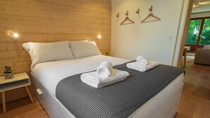 Une chambre moderne avec un grand lit, une table de chevet agrémentée d’une plante, et une vue sur l’extérieur grâce à une porte coulissante.