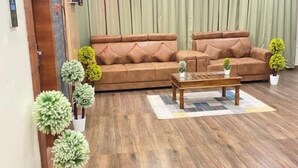A living room with a brown sofa, a wooden coffee table, and potted plants. - PPH Living Gnr Grand Luxury Rooms (Madanapalle)