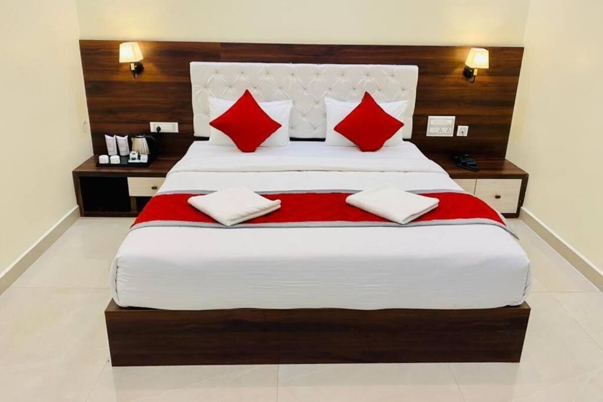A neatly made bed with a wooden headboard, two red pillows, and a white bedspread. There are two bedside tables with lamps and a small tray of toiletries.