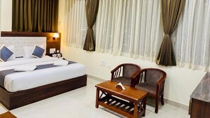 A hotel room with a bed, two chairs, a table, and curtains. - PPH Living Gnr Grand Luxury Rooms (Madanapalle)