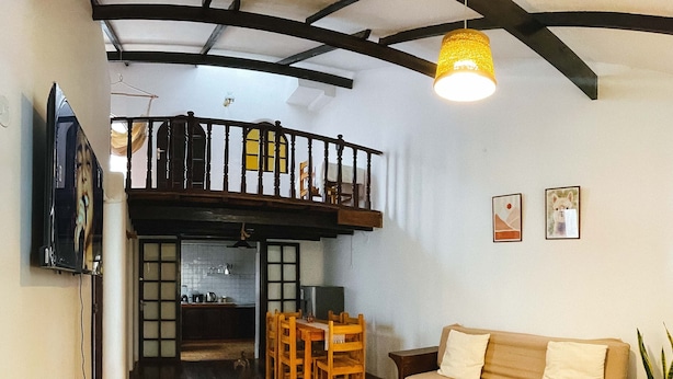 A living room with a sofa, coffee table, and a dining area with chairs. There is a balcony with a railing and a hanging light fixture. - COZY HOME CUSCO (Cusco)