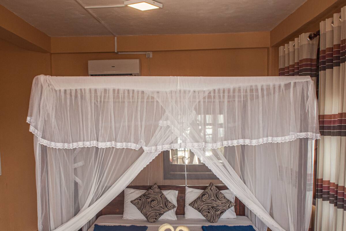 A bed with a canopy, blue bedspread, and two swan-shaped pillows.