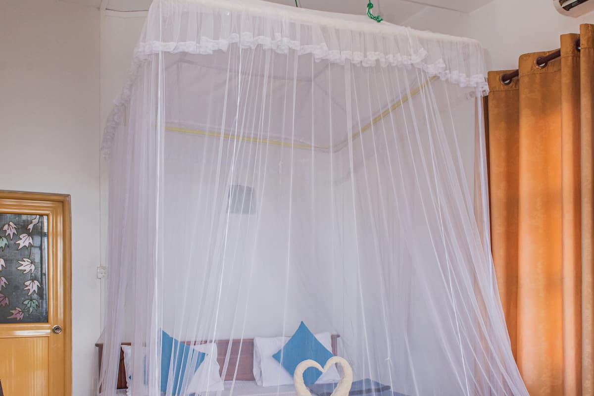 A bedroom with a four-poster bed, a wooden headboard, a white canopy, and a wooden door with a glass panel.