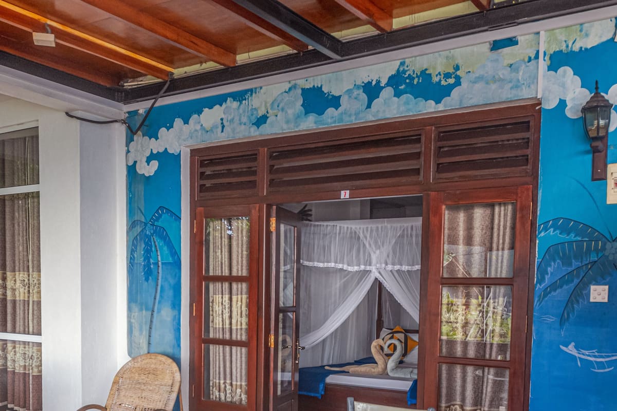 A room with a round table and four chairs, a window with curtains, and a mural on the wall.