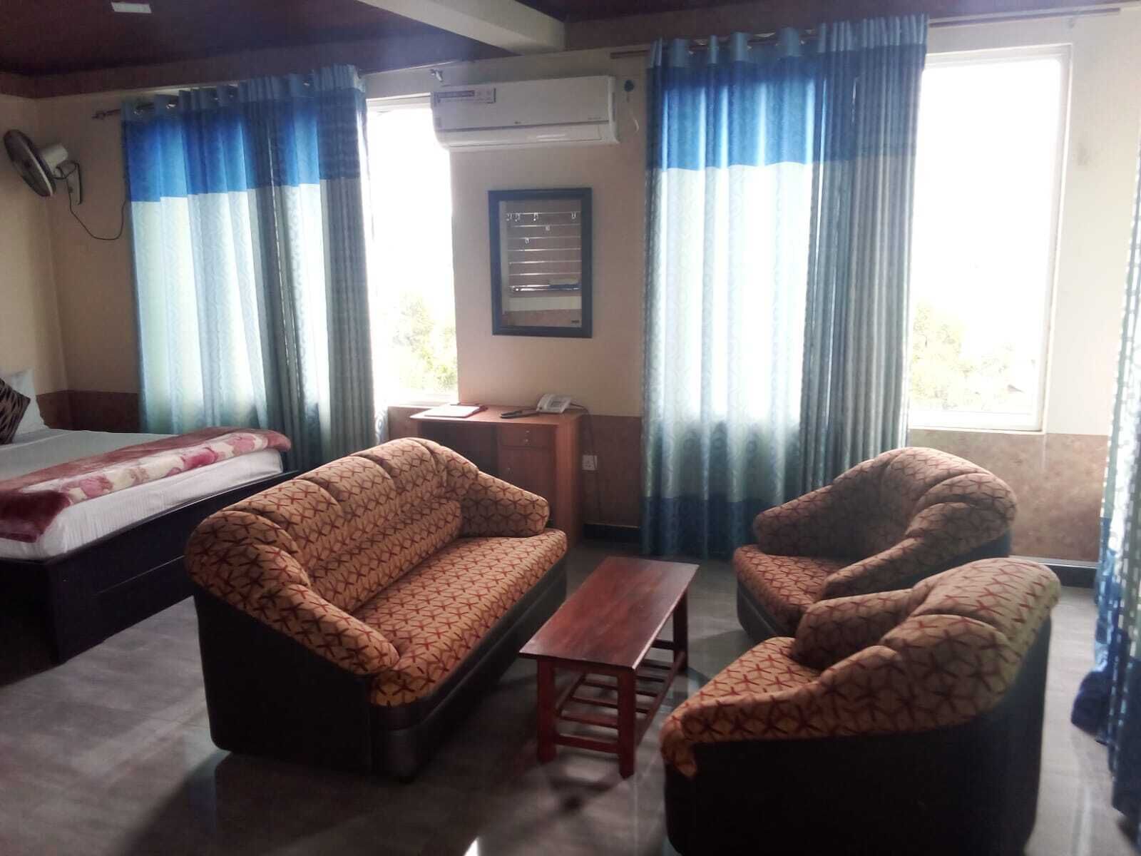 A hotel room with a bed, a sofa, a chair, a small table, and a desk with a telephone.