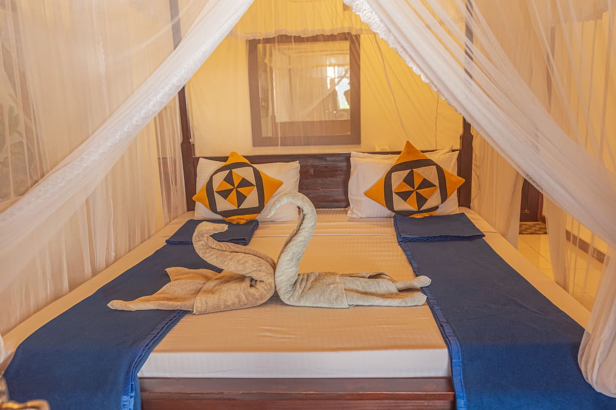 A bed with a canopy, two pillows with geometric patterns, and two swan-shaped pillows.