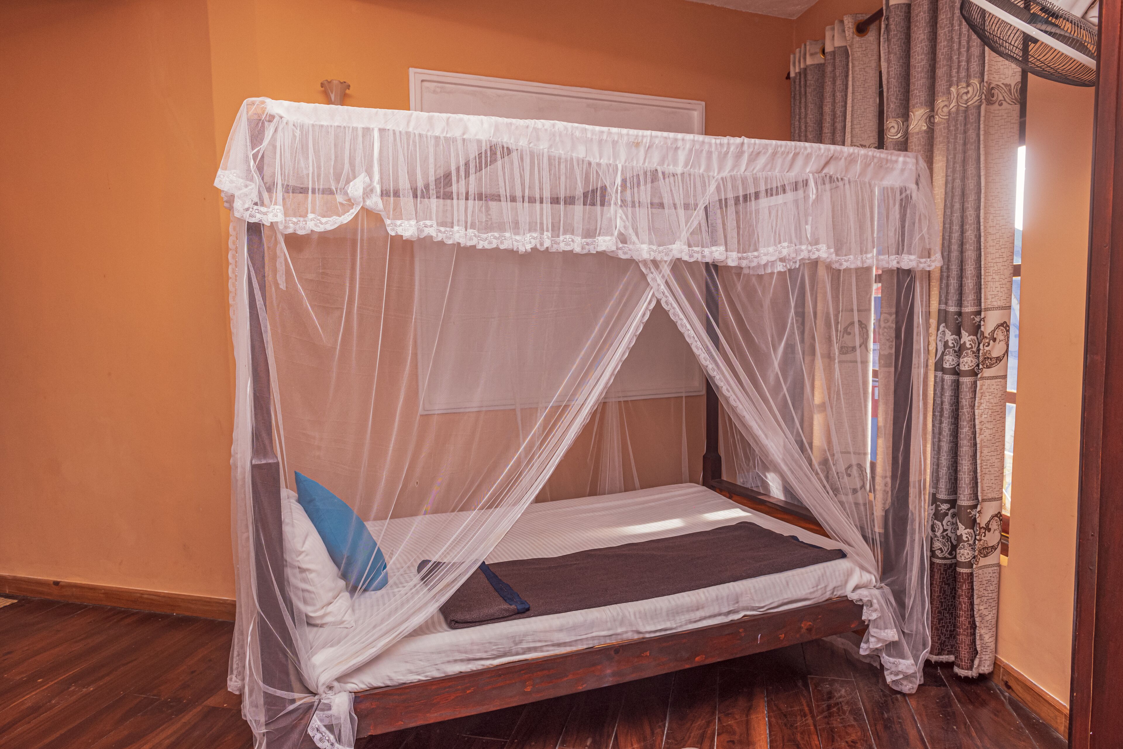 A single bed with a canopy, a wooden floor, and a window with curtains.