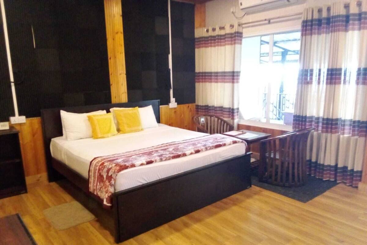 A bedroom with a wooden bed, a nightstand, a desk, and a window with curtains.