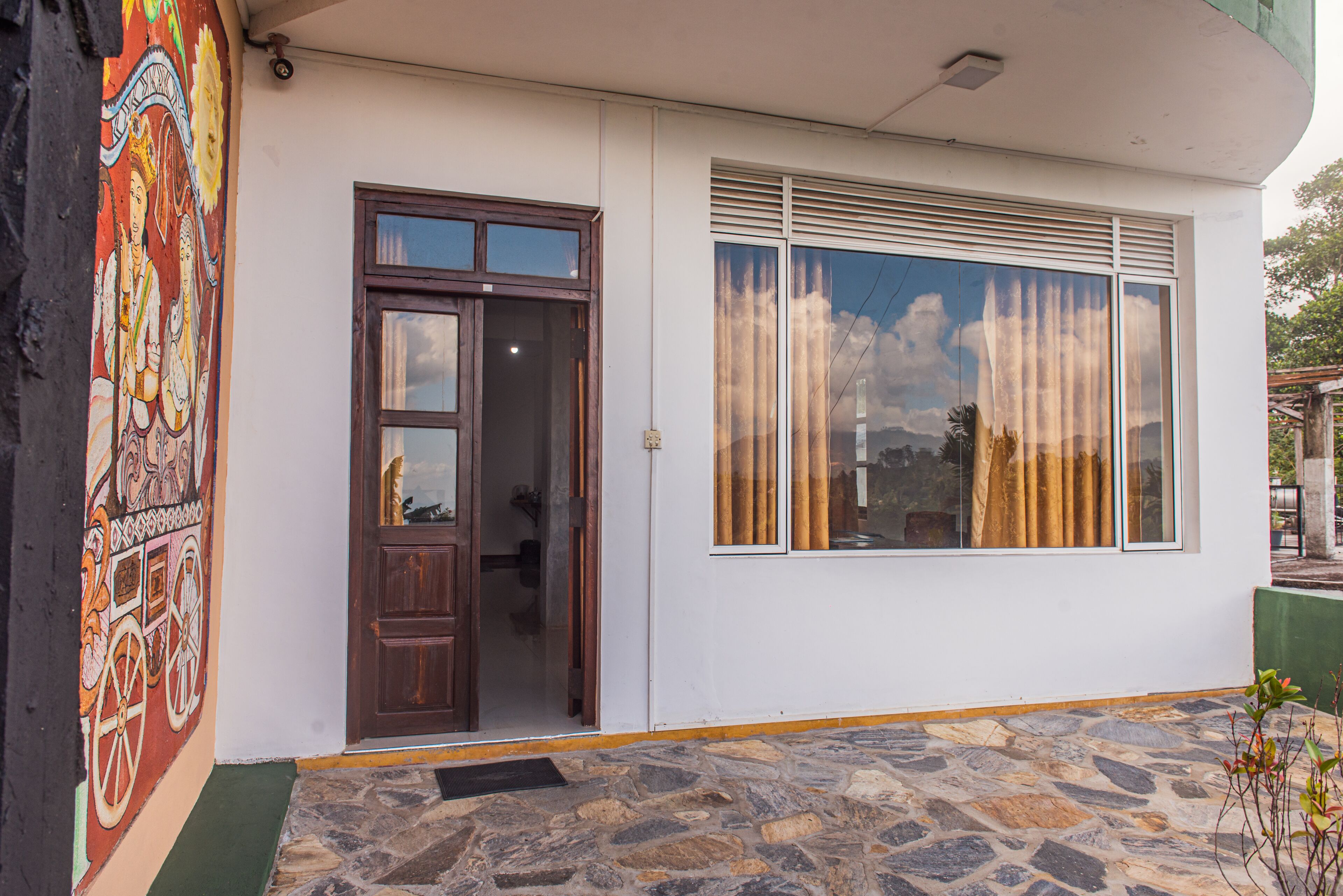 A building with a stone-paved entrance, a wooden door, and a window with blinds.
