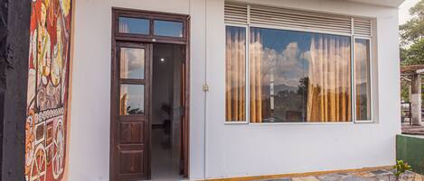 A building with a stone-paved entrance, a wooden door, and a window with blinds.