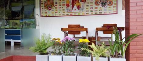 Un área de recepción con un mural de banderas, bancos de madera y plantas en macetas.