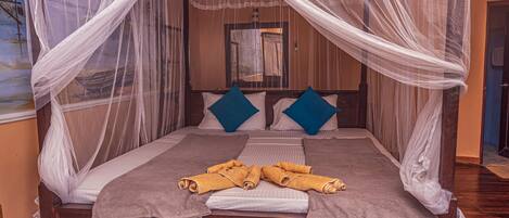 A four-poster bed with a canopy, two blue pillows, and rolled towels on the bed.
