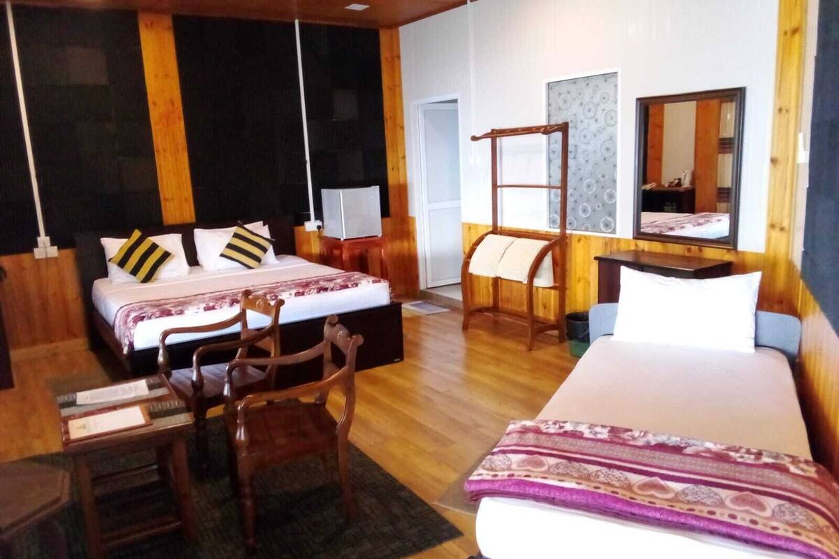 A hotel room with a large bed, a smaller bed, a desk, and a chair. There is a mirror on the wall and a window with a view.