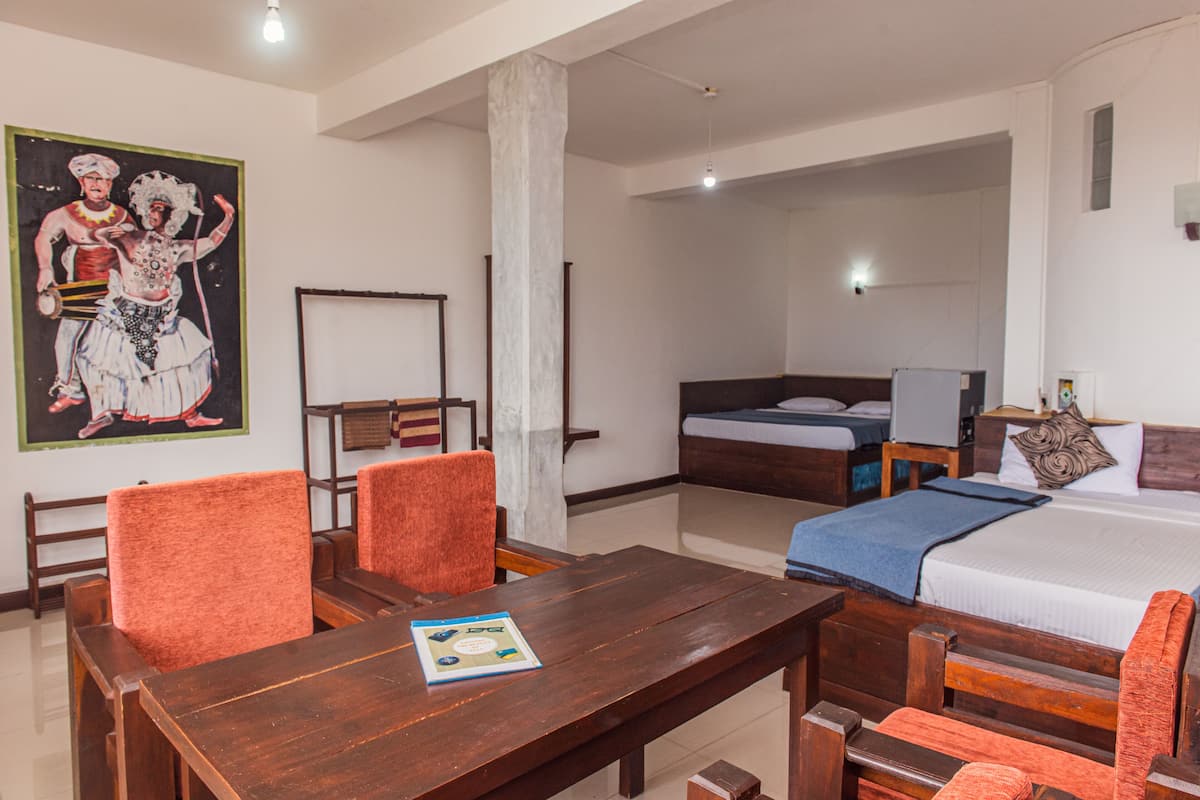 A hotel room with a wooden table, orange chairs, a bed with a blue blanket, and a painting on the wall.