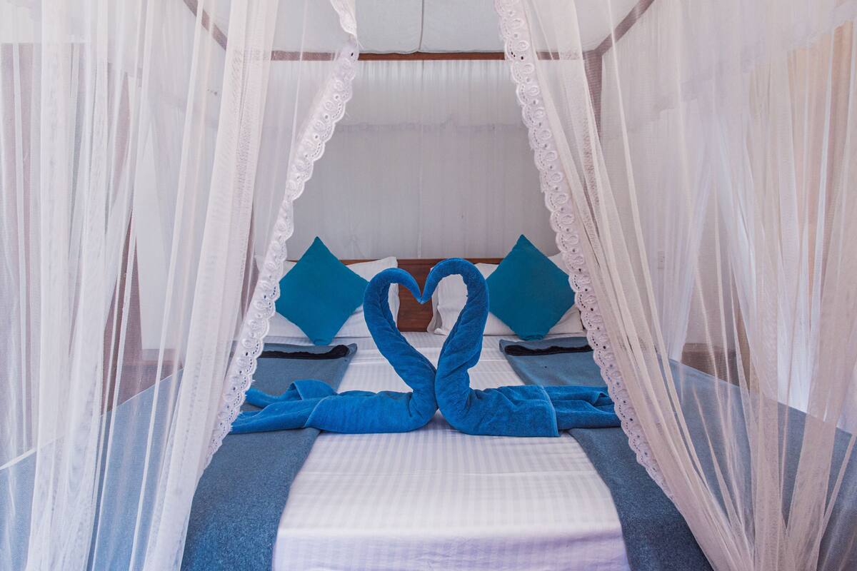 A bed with a canopy, two pillows, and a heart-shaped towel arrangement.
