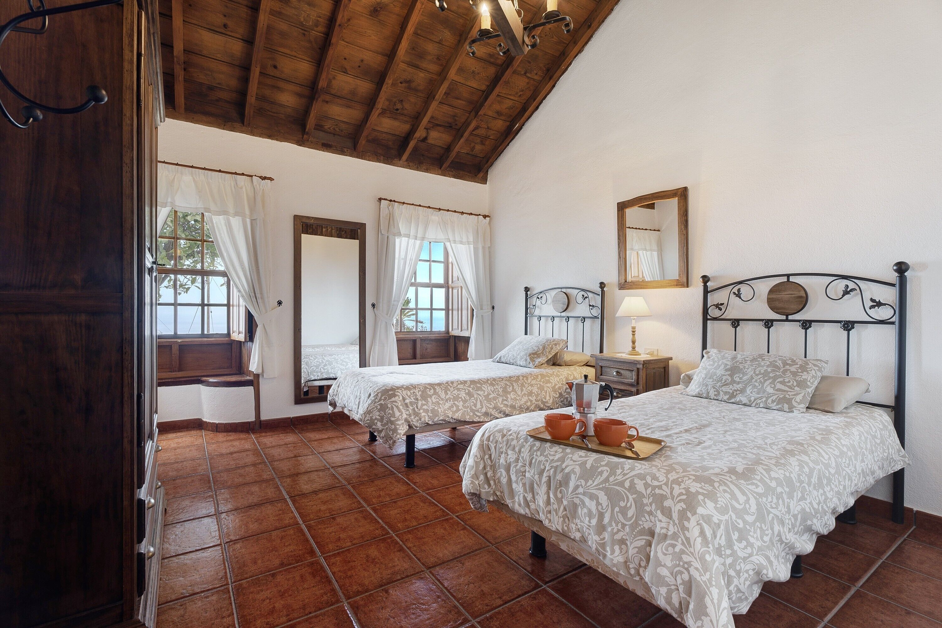 A bedroom with two beds, a wooden ceiling, and a tiled floor.