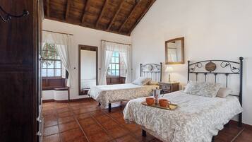 A bedroom with two beds, a wooden ceiling, and a tiled floor.