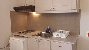 Kompakti keittiö, jossa on valkoiset kaapit, sisäänrakennettu liesi ja pesuallas.