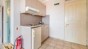 Cucina con fornello, lavello e pensili, estintore e una porta con cartello verde.