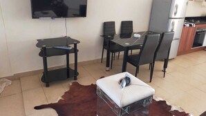 Un coin repas avec un téléviseur fixé au mur, une table à manger avec des chaises, un réfrigérateur et un espace cuisine.