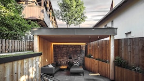 A covered outdoor seating area with a stone wall, wooden deck, and a black metal chair. - Rousa Little Guesthouse Cosy – Breakfast Included! (Rasun Anterselva)
