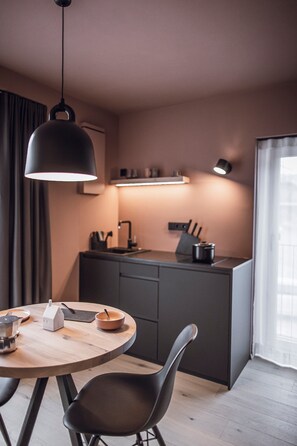 Une cuisine moderne avec une table et des chaises, un luminaire suspendu et une fenêtre avec des rideaux.