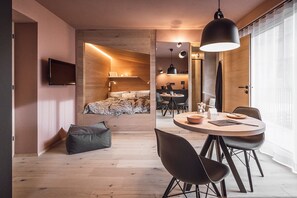 A modern hotel room with a bed, a dining area, a TV, and a large window. - Rousa Little Guesthouse Cosy Plus – Breakfast Included! (Rasun Anterselva)