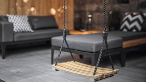 Un interior de madera con una mecedora colgante, sofá gris y pared de piedra.