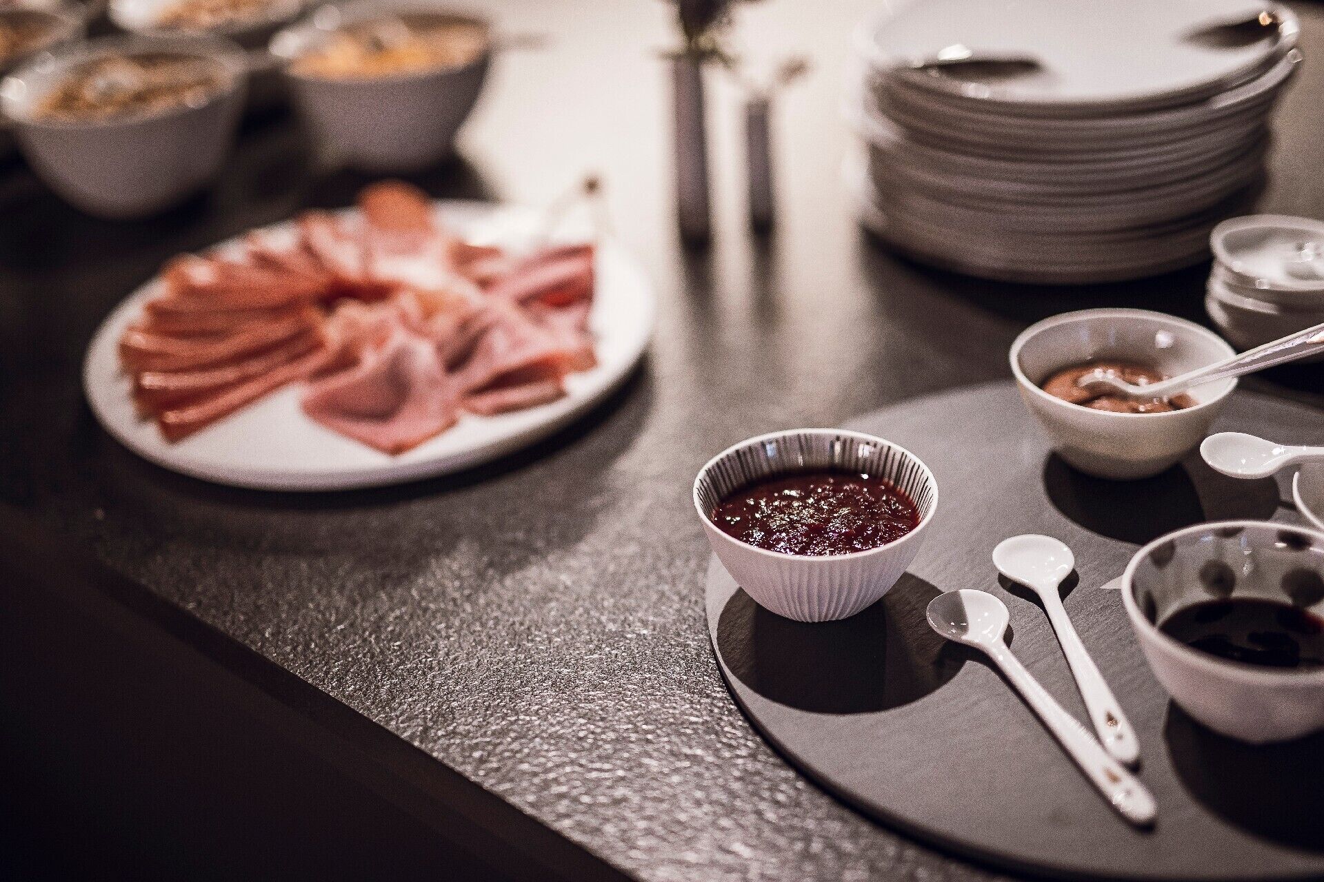 A dining table with plates of food, bowls, and spoons.