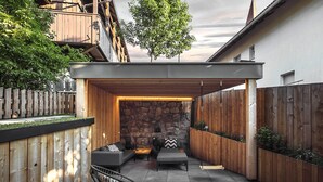 Un espacio de estar al aire libre con techo, una pared de piedra, cubierta de madera y una silla de metal negro.